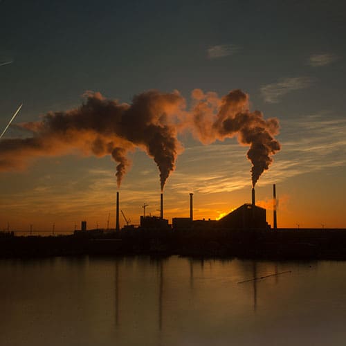 Low angle shot of a factory with smoke and steam coming out of the chimneys captured at sunset